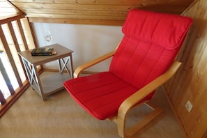 A wooden-framed room with a red cushioned chair, a small table with a book and a glass of water, and a window with natural light. - Holiday home with 3 bedrooms (Boltenhagen)
