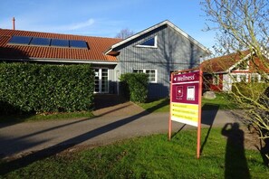 A building with a sign indicating a wellness center, a red-tiled roof, and a pathway leading to the entrance. - Holiday home with 3 bedrooms (Boltenhagen)