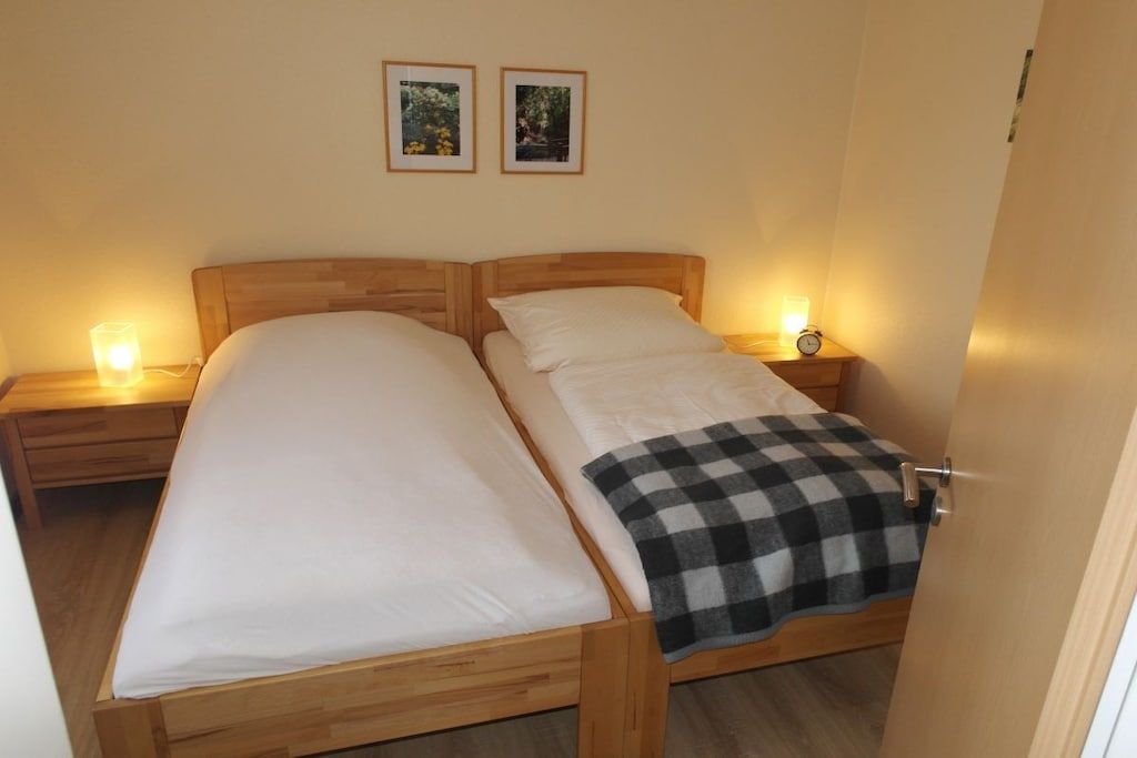 Ein Doppelbett mit karierter Tagesdecke, Nachttischlampen und zwei gerahmte Bilder an der Wand.