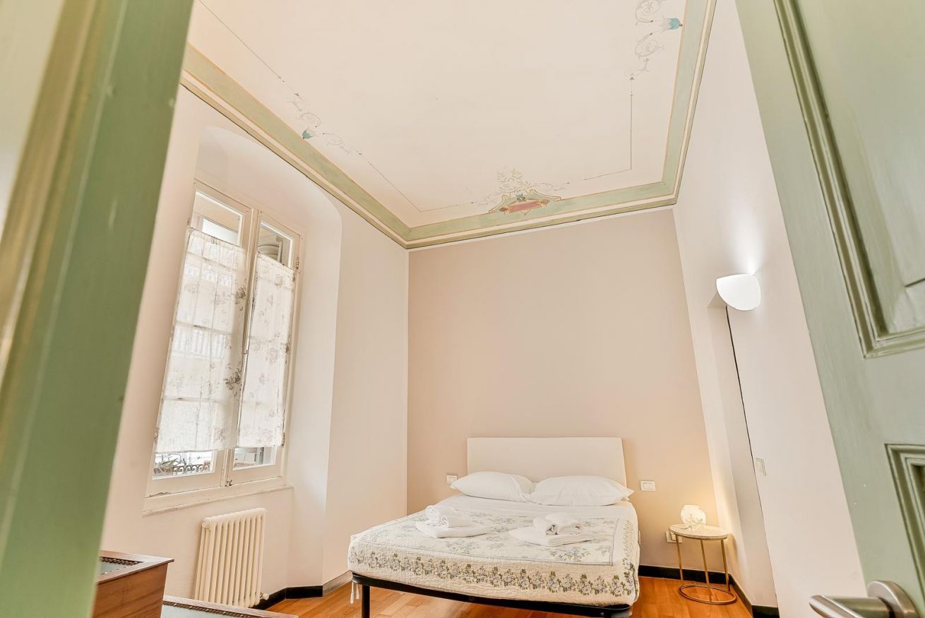 Een slaapkamer met een bed, een radiator, een raam met gordijnen en een deur.