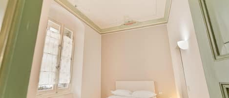 Une chambre à coucher avec un lit, un radiateur, une fenêtre avec des rideaux et une porte.