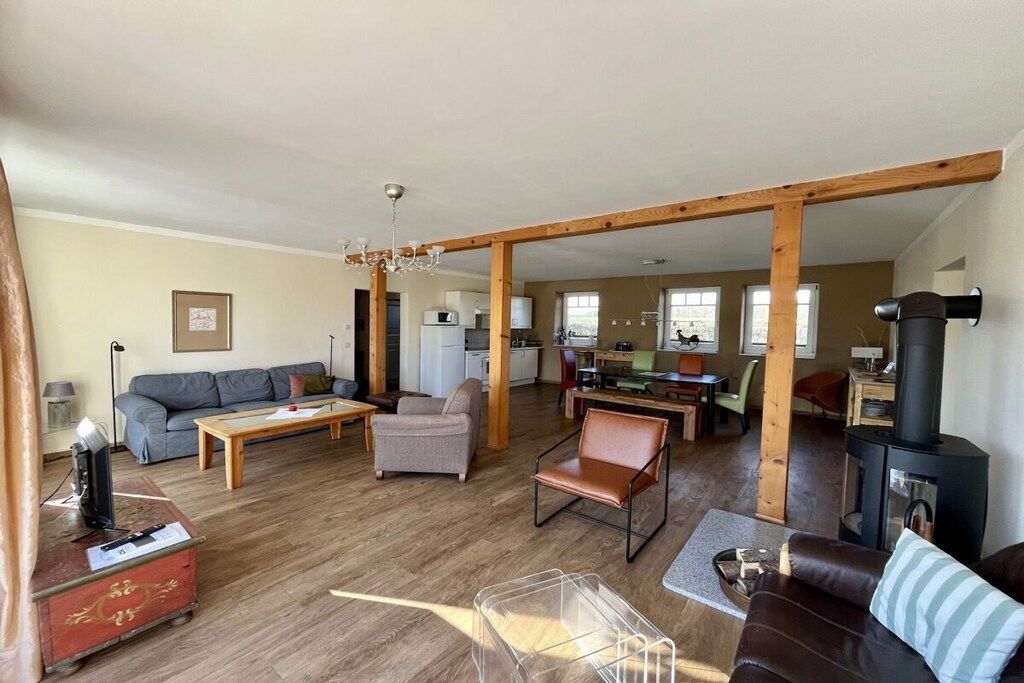 Ein großzügiger Wohnbereich mit Holzboden, einer Couch, einem Couchtisch, einem Kamin und einer Küche im Hintergrund.