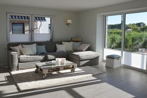 A modern living room with a sectional sofa, a glass coffee table, and a view of greenery outside. - Holiday apartment with 2 bedrooms (Kronsgaard)
