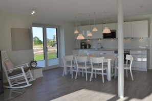 A modern kitchen with white cabinets, a dining area with white chairs, and pendant lights. - Holiday apartment with 2 bedrooms (Kronsgaard)