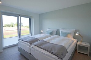 Une chambre avec un grand lit, deux tables de chevet et une vue sur l’extérieur, accessible par une porte coulissante.