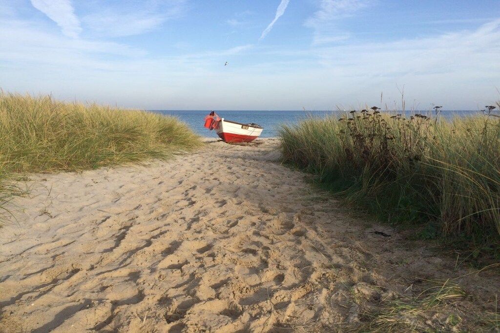 Een zandpad langs het strand dat leidt naar een klein bootje, met een persoon in de buurt.