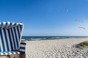 Une plage avec une chaise de plage à rayures et des mouettes qui volent.
