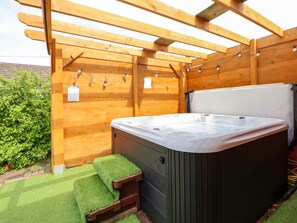 Ein Whirlpool unter einer hölzernen Pergola mit einer Rasenfläche davor.