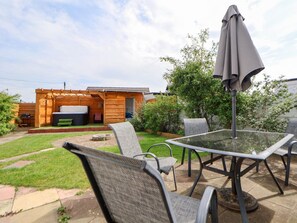 Eine Terrasse im Freien mit einem Tisch aus Glas und Metallstühlen, ein Holzdeck und ein Whirlpool.