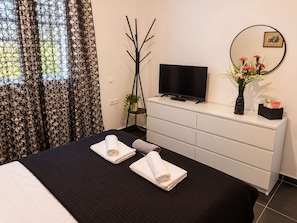 Ein Hotelzimmer mit einem Bett, einem Flachbildfernseher, einem Schminktisch und einem Fenster mit gemusterten Vorhängen.
