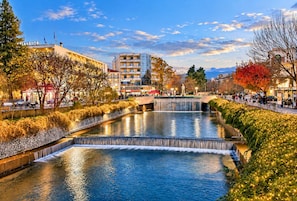A riverside walkway with a waterfall, buildings, and trees. - Tania's House - Meteora Peaceful Garden Retreat (Flamouli)