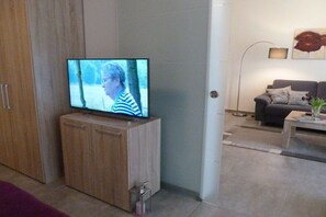 Ein Fernseher steht auf einer Holzkommode in einem Wohnzimmer mit einer Couch und einer Stehlampe.