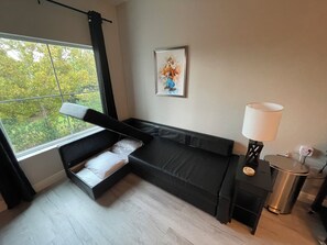 Una camera moderna con un letto, un tavolino, una lampada e una finestra vista alberi.