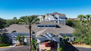 A multi-story hotel with a covered parking area, palm trees, and a red car parked in front.