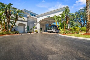 A hotel entrance with a covered driveway, palm trees, and a bus. - King & Queen Beds! FREE SHUTTLE * FREE PARKING * No Resort Fee * Coffee Bar * Waffle Bar * 76" & 70" Smart TV's * Pool & Hot Tub * Plush Towels & Linens * Gas BBQ Grill * King Bed Has Adjustable Base * Sleeper Sofa * 2 Mile to Disney Springs *7 Mile (Orlando)