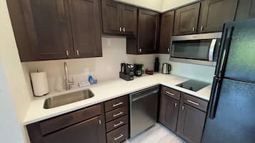 A compact kitchen with dark wooden cabinets, a stainless steel sink, a black refrigerator, and a microwave.