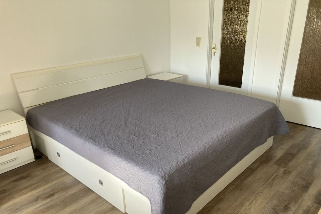 A single bed with a headboard, a bedside table, and a wardrobe in a room with wooden flooring.
