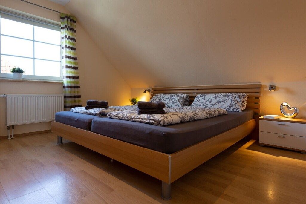 Ein modernes Schlafzimmer mit einem hölzernen Bett, einem Nachttisch, einer Heizung und einem Fenster mit Vorhängen.