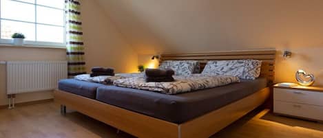 Ein modernes Schlafzimmer mit einem hölzernen Bett, einem Nachttisch, einer Heizung und einem Fenster mit Vorhängen.