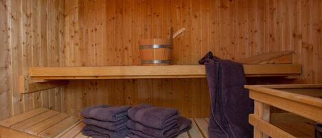 A wooden sauna with a wooden bench, a stack of towels, and a wooden bucket.