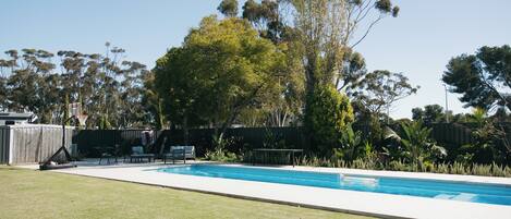 Una piscina rectangular con zona verde alrededor y una terraza de madera.