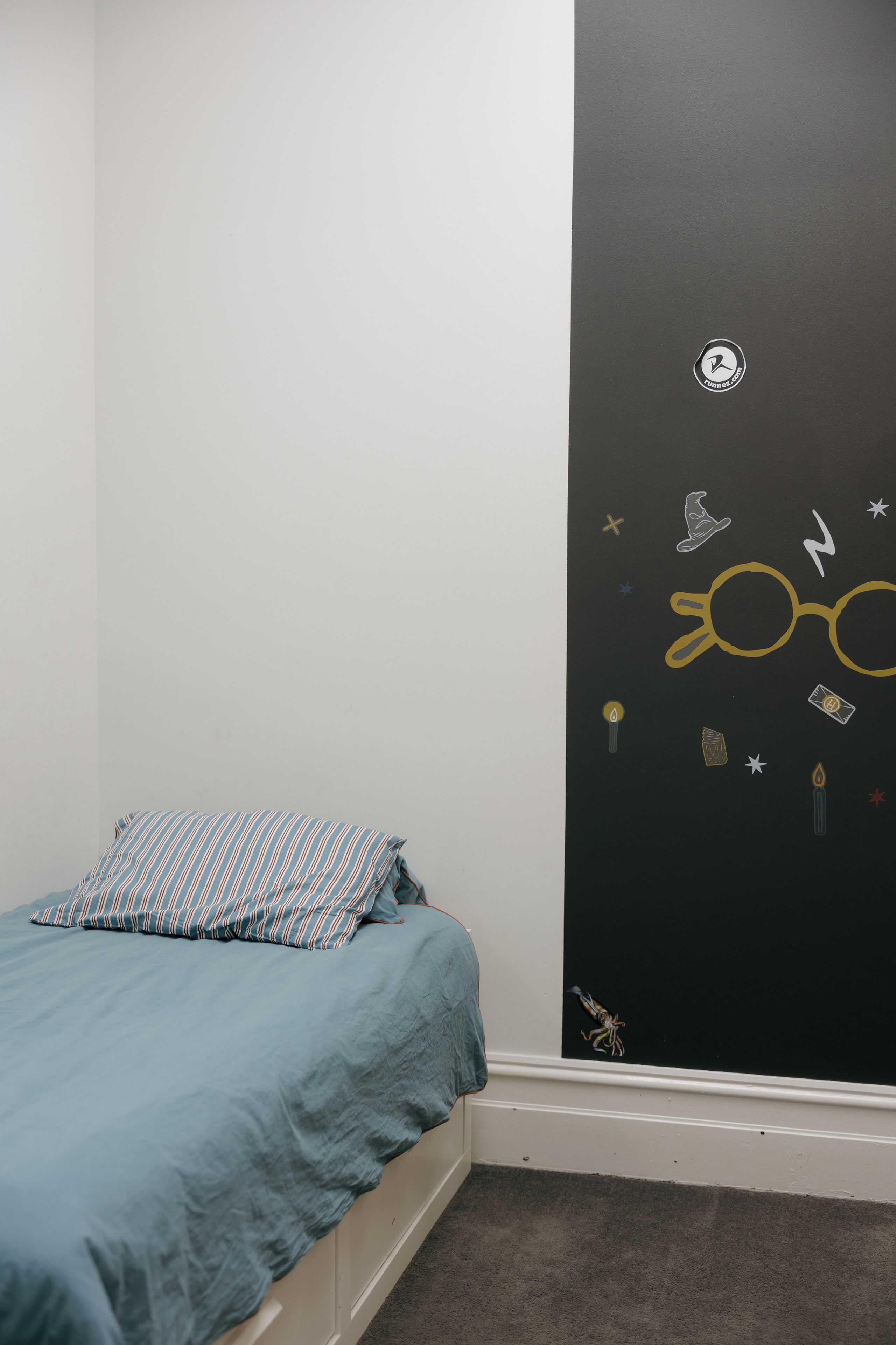 Un dormitorio con una cama, una pared con un diseño negro y una ventana pequeña.