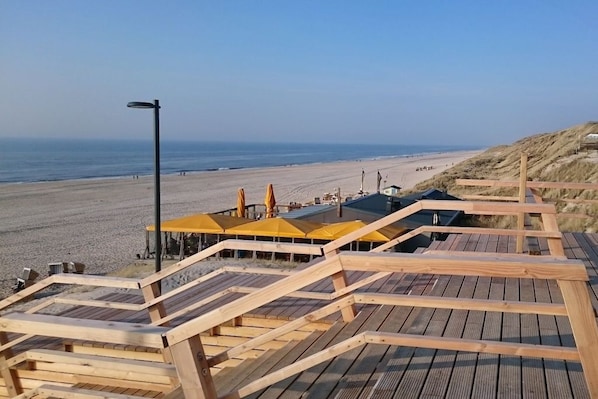 A wooden boardwalk leading to beach umbrellas and a building with a sloped roof. - No. 03 in the Atlantic House (Wenningstedt)