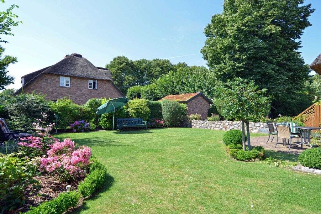 Ein Wohnhaus mit gepflegtem Rasen, einer Terrasse und Gartenmöbeln sowie einem großen Baum, der Schatten spendet.