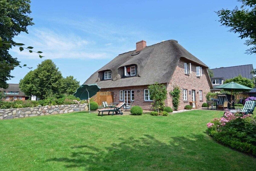Ein Haus mit einem Reetdach, einer Steinsäule und einem gepflegten Rasen.