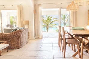 A room with a dining area, a wicker sofa, and a view of the ocean. - Oceanfront Villa - East Coast, Private beach & Pool (Quatre Cocos)