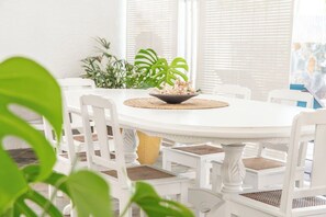 A round dining table with white chairs, a central bowl with decorative items, and a potted plant in the background. - Oceanfront Villa - East Coast, Private beach & Pool (Quatre Cocos)