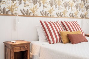A bedroom with a bed, two pillows, a bedside table, and a wall with floral wallpaper. - Oceanfront Villa - East Coast, Private beach & Pool (Quatre Cocos)