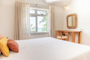 Ein Schlafzimmer mit einem Bett, einem Schreibtisch, einem Stuhl, einem Fenster mit Vorhängen und einem Spiegel an der Wand.