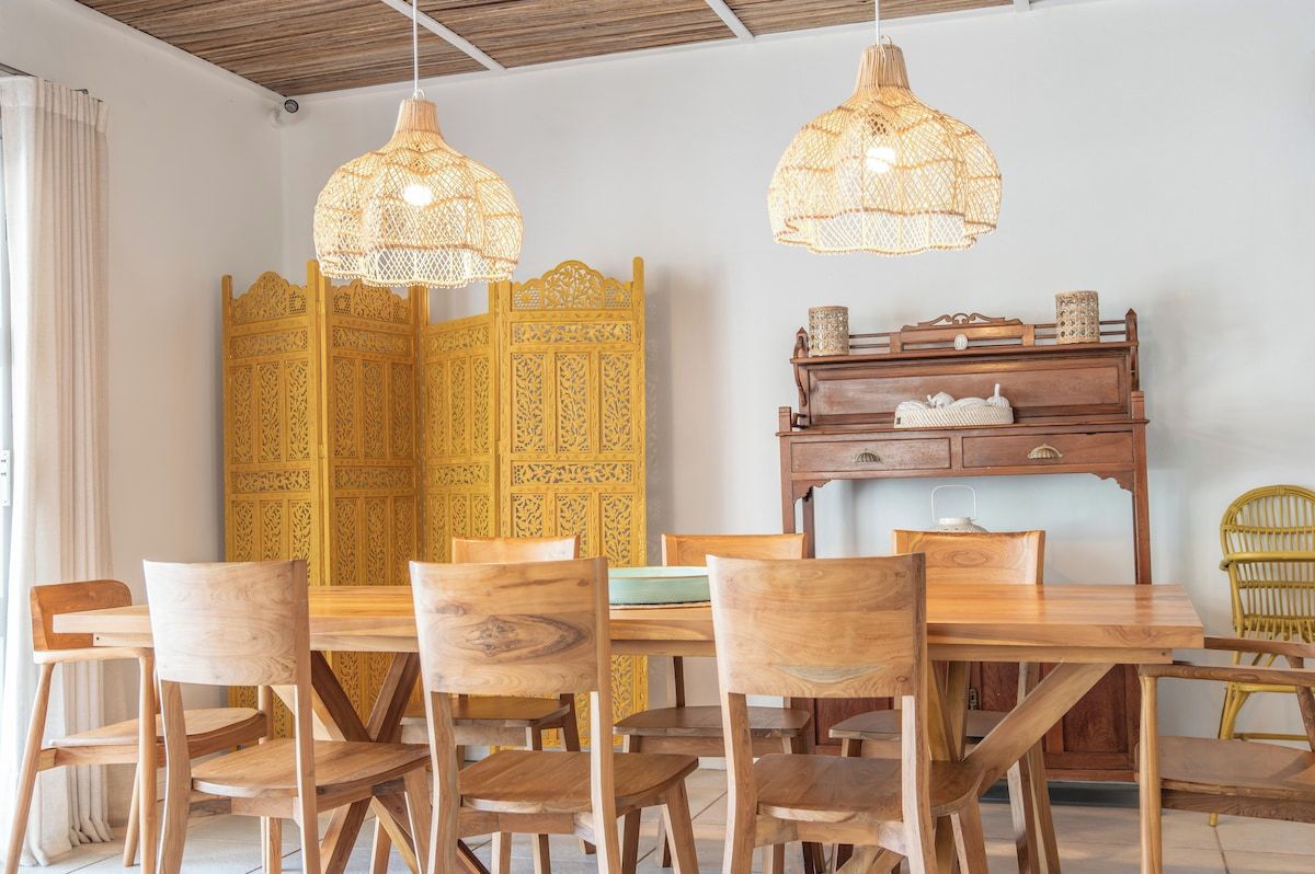 A dining area with a wooden table and chairs, a decorative yellow partition, and hanging wicker lamps.