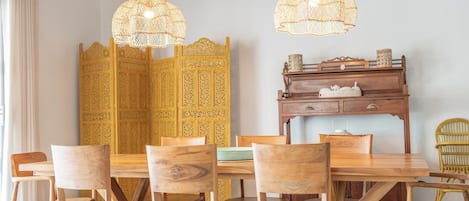 Un espace repas avec une table et des chaises en bois, un paravent jaune décoratif et des lampes suspendues en osier.