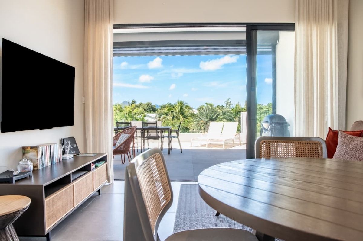 Een moderne hotelkamer met een flatscreen-tv, een eethoek met een ronde tafel en een balkon met buitenmeubilair.