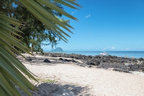 Ein Strand mit felsiger Küste, einem Boot und einem Berg im Hintergrund.