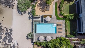 Eine Vogelperspektive eines Resorts mit Schwimmbad, Liegestühlen und Strand.