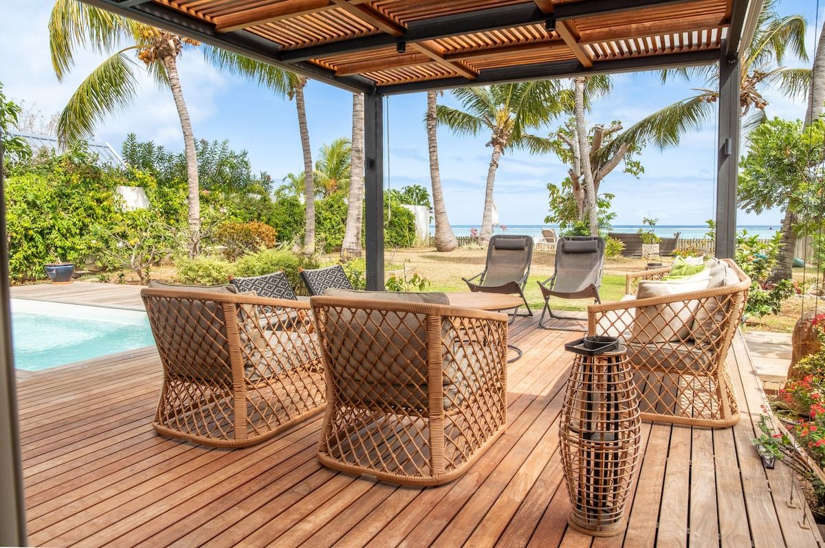 Une terrasse en bois avec des meubles en osier, une piscine et une vue sur l’océan.