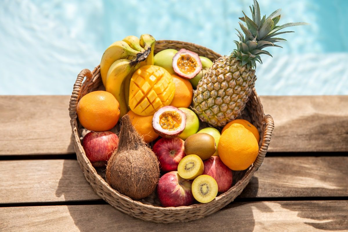 Ein Korbwesen-Korb, gefüllt mit verschiedenen Früchten und einer Ananas auf einer Holztischplatte.