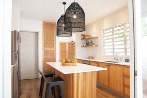 Une cuisine moderne dotée d’un îlot central, de meubles en bois et de luminaires suspendus noirs.