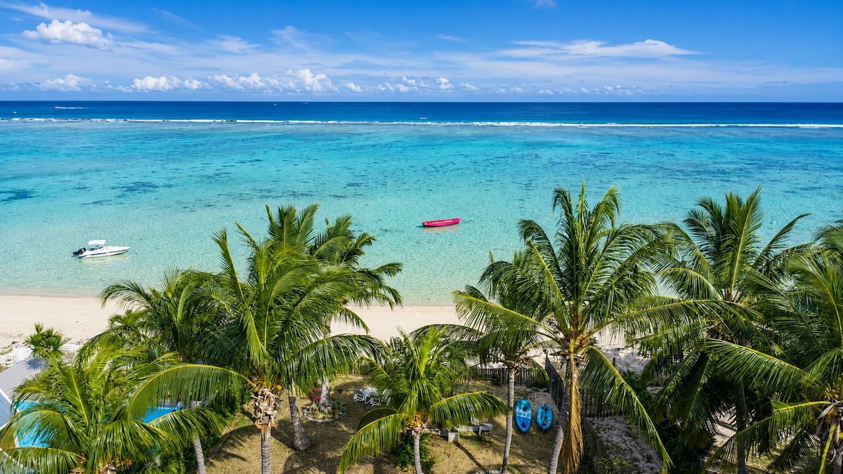 Ein Strand mit klarem türkisblauem Wasser, einem weißen Boot und Palmen.