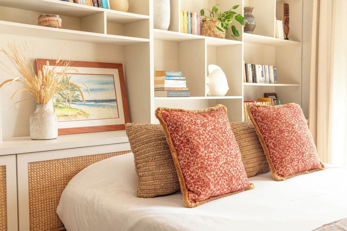 Een slaapkamer met een bed, een boekenkast vol boeken en decoratieve objecten, en een schilderij aan de muur.