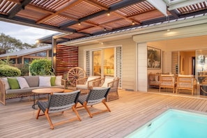 Eine Holzterrasse mit Gartenmöbeln, einem Pool und einer überdachten Patio-Ecke.