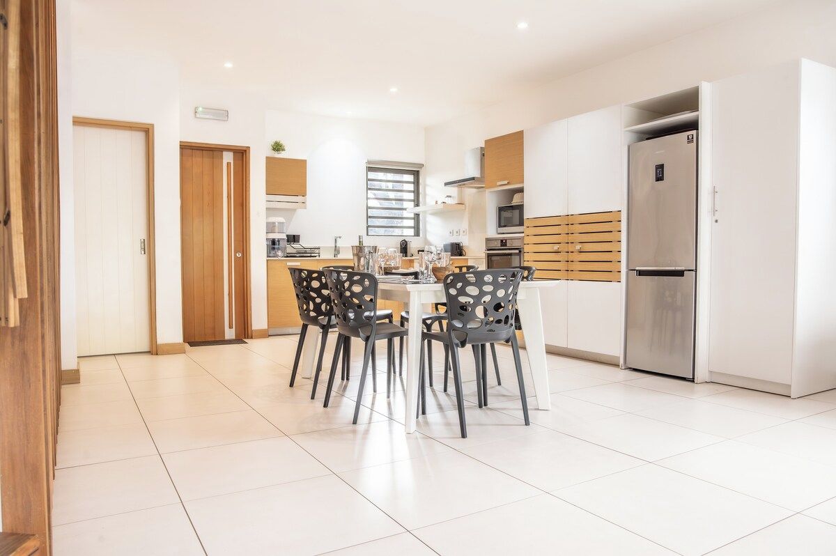 Una cocina moderna con comedor, que incluye una isla central, electrodomésticos integrados y un refrigerador grande.