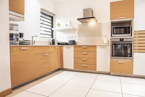 A modern kitchen with wooden cabinets, a built-in microwave, and an oven. - Amazing Sunsets & Plunge Pool - Walk to Everything (Grande Riviere Noire)