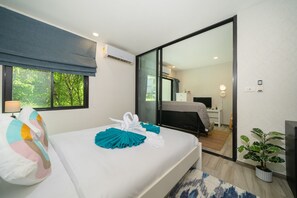 Habitació d'hotel amb un llit, una finestra amb vistes a arbres, un escriptori amb un ordinador i una planta en test.