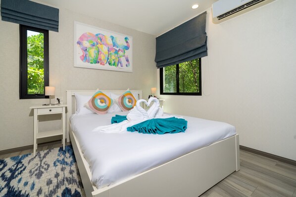 A hotel room with a bed, a bedside table, a lamp, a painting, and a window with a view of greenery. - Direct Pool Access - Modern 1BR - 104 @ The Title - Walk to Beach & Airport (Sakhu)