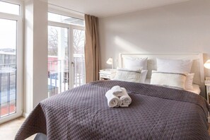 A hotel room with a large bed, a window with a view, and a bedside table with a lamp. - Holiday apartment with 1 bedroom (Lübeck Travemünde)