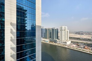 A modern high-rise building with a glass facade reflecting the sky and surrounding structures. - Trillionaire 1BR Trendy Timeless Tempting (Dubai)